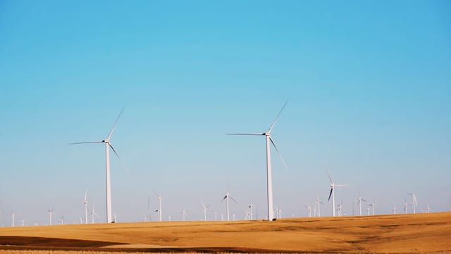 High wind power plant generating electricity located on flat desert sandy area against cloudless blue sky