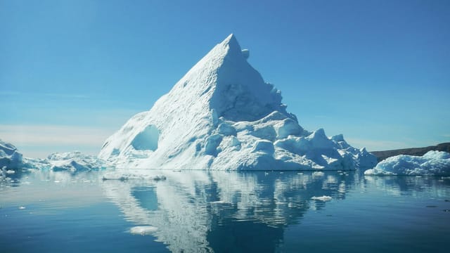 Stunning view of a towering iceberg reflecting in the calm waters of Tiniteqilaaq, Greenland.