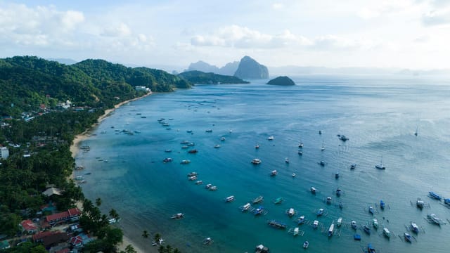 Stunning aerial view of El Nido's vibrant blue bay with lush greenery and boats, capturing the essence of the Philippines' natural beauty.