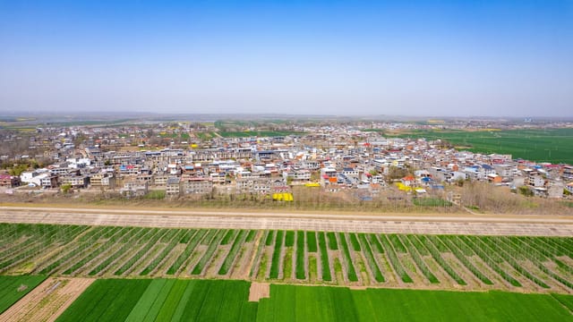 Aerial shot showcasing An Qing Shi village and expansive farmlands under a clear blue sky.