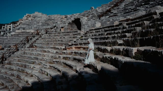 A woman in a white dress walks through the ancient theatre ruins in Kaş, Antalya.