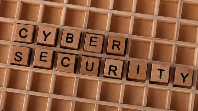 Wooden letter blocks spelling 'CYBER SECURITY' on a wooden grid background for data protection themes.