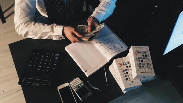 Businessman organizing finances with tech devices and cash on desk.