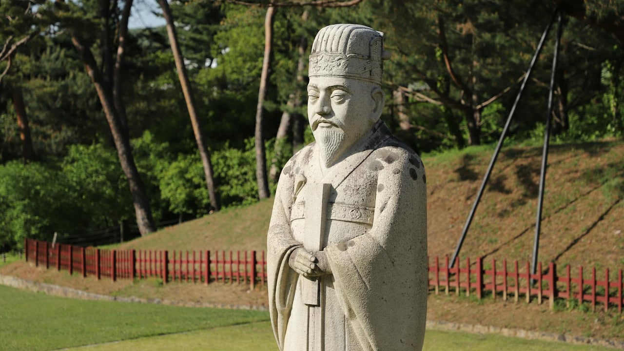 Stone statue of a historical figure in a green park with trees and grass on a sunny day.