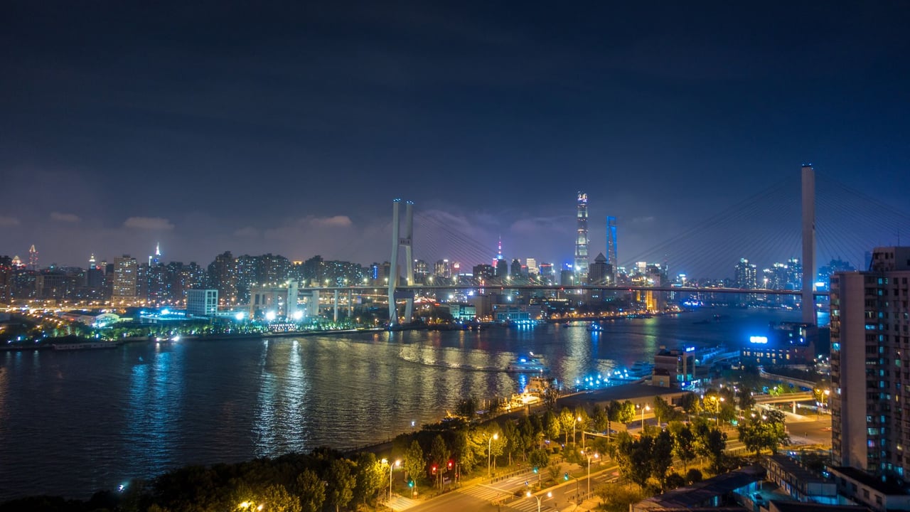 Illuminated cityscape with skyscrapers reflecting on a river at night, showcasing urban architecture.