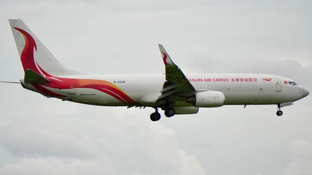 Side view of a Tianjin Air Cargo plane flying in a cloudy sky.