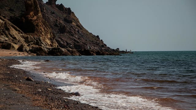 Waves crash on the rocky shore of Hormoz Island, Iran with clear blue skies.