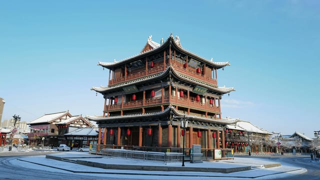 Red pagoda in a snowy cityscape with blue skies, showcasing traditional Asian architecture.