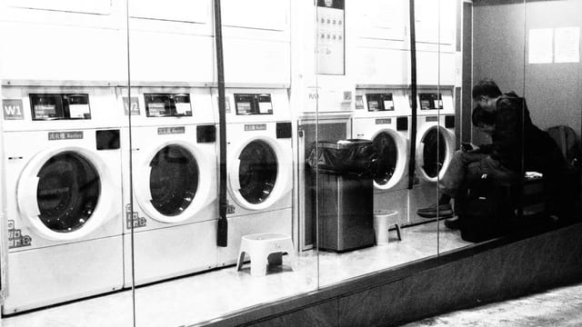 A black and white photo capturing a quiet moment inside a Hong Kong laundromat at night.