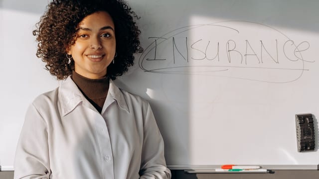 Illustrative image: African American woman smiling in office setting with a whiteboard displaying 'Insurance'.