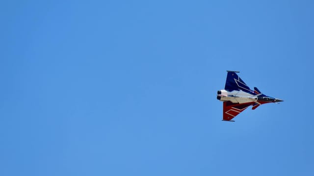 Jet fighter executing precise aerobatic maneuvers against a clear blue sky in Le Bourget, France.