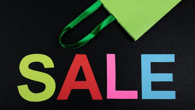 Close-up of colorful SALE letters on black background with green shopping bag.