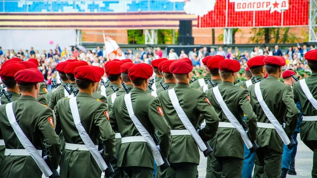 Back view of soldiers in green military uniforms and red berets during a parade.