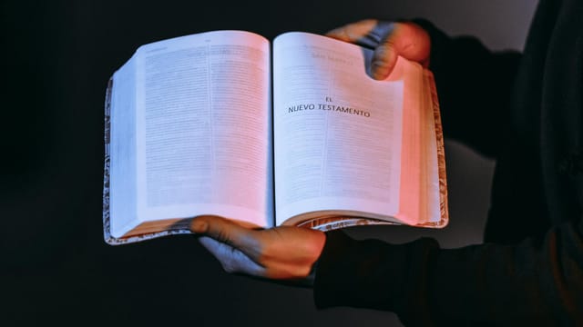 A person holds an open Bible showcasing the New Testament under dramatic lighting.