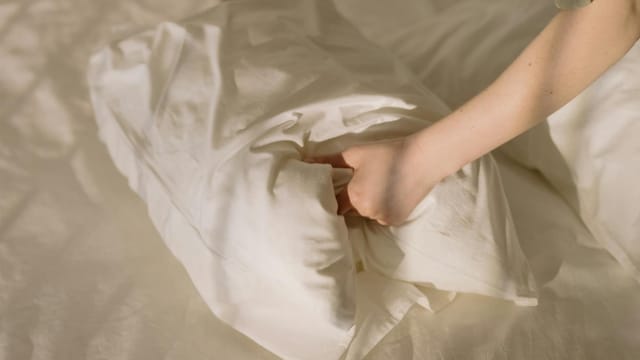 Close-up of clean white linens in a cozy bedroom setting, emphasizing comfort and cleanliness.