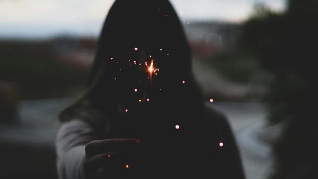 A person holds a sparkler at twilight, creating a magical and mysterious silhouette effect.
