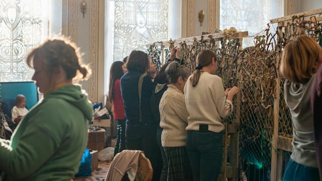 A group of women indoors creating camouflage nets, emphasizing community support and collaboration.