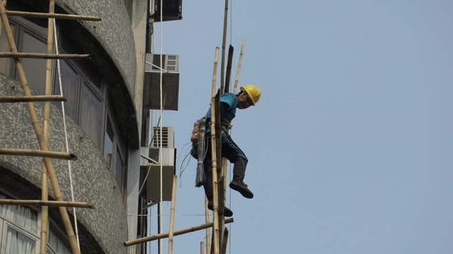 Construction worker on bamboo scaffolding in Hong Kong, showcasing traditional techniques.
