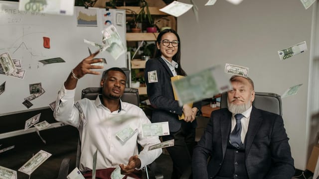 Diverse business team celebrating success with cash raining indoors in office.