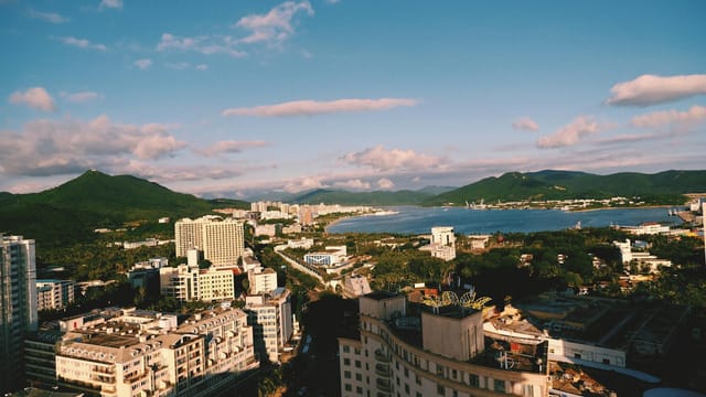 A breathtaking aerial view of a coastal city with mountains in the background under a clear blue sky.