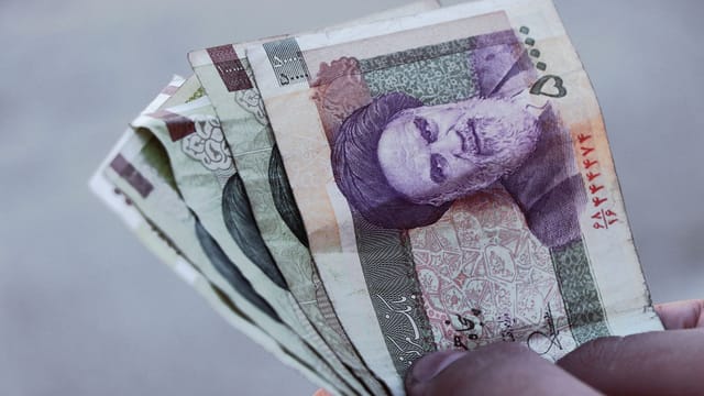 Detailed view of Iranian rial banknotes held in hand, illustrating finance and economy in Iran.