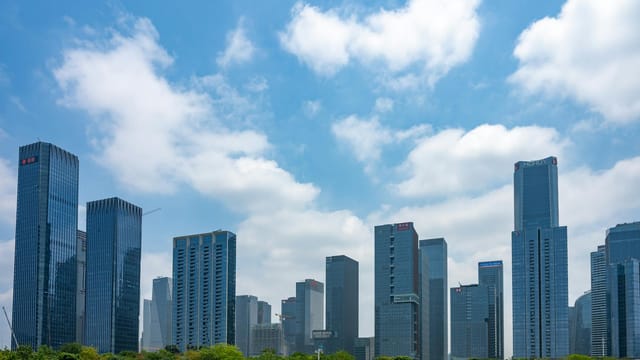 Skyscrapers in Shenzhen, China under a vibrant blue sky with fluffy clouds, showcasing urban architecture.
