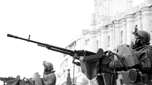 Monochrome image of soldiers in armored tanks, equipped with rifles, patrolling urban surroundings.