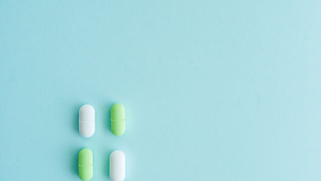 Four pills, green and white, arranged on a vibrant blue background.