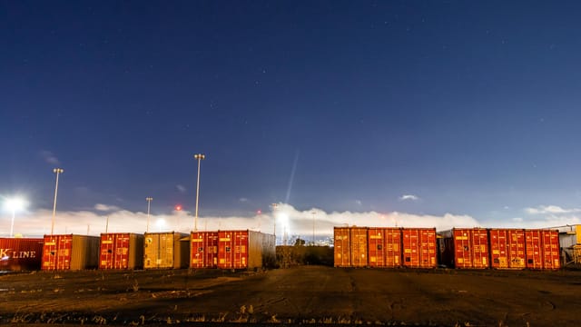 Stacked shipping containers on industrial site with star-filled night sky backdrop.
