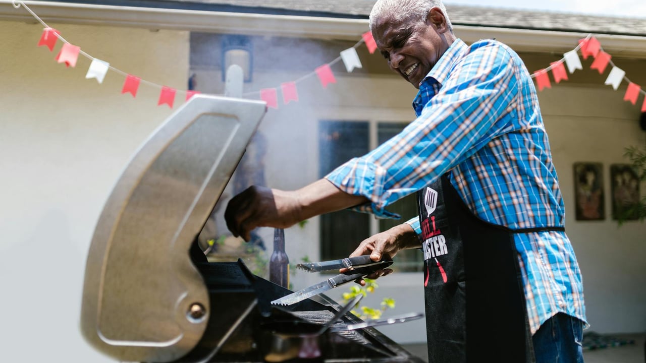 Senior man barbecuing outside on a sunny day, enjoying cooking on a grill.