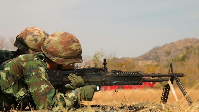 Two soldiers in camouflage uniforms practicing on a field with a machine gun in combat training.
