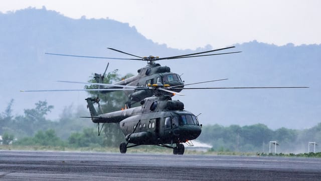 Modern armed military helicopters landing on asphalt ground against rocky hills in countryside on daytime