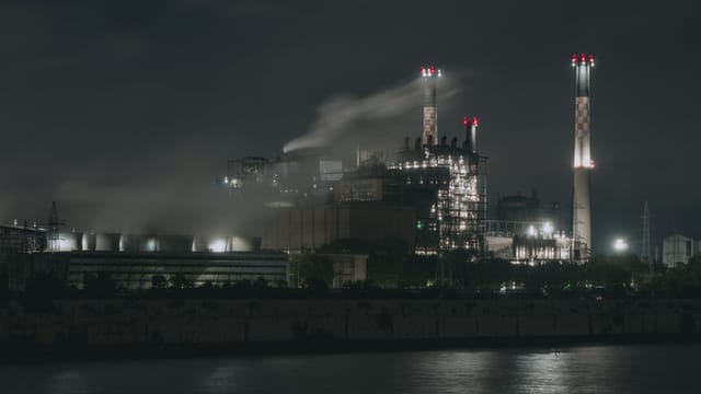 Night view of a large industrial factory with chimneys emitting smoke by the river in Ahmedabad, India.