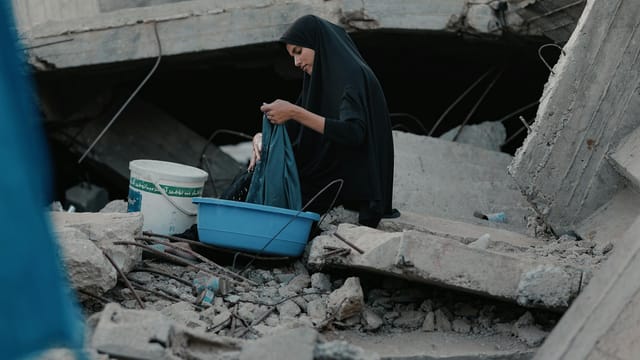 A woman in Gaza washes clothes amidst the rubble, highlighting resilience and survival.