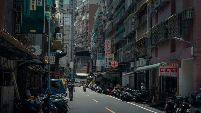 A bustling urban street with lined motorcycles and towering old buildings.