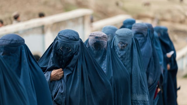 A group of women covered in blue burqas walking outdoors in Afghanistan, highlighting cultural attire.
