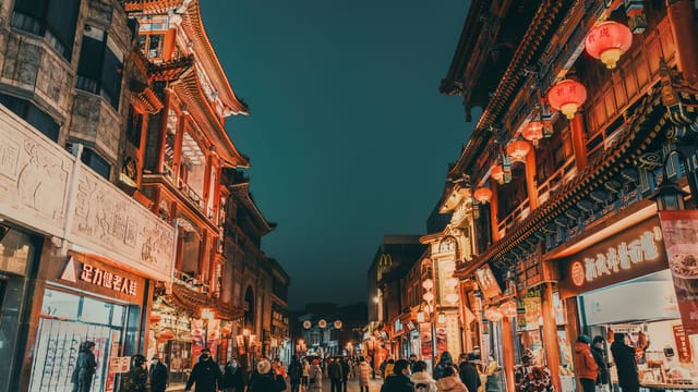 Lively urban scene of a Chinese street at night with traditional architecture and bustling crowd.