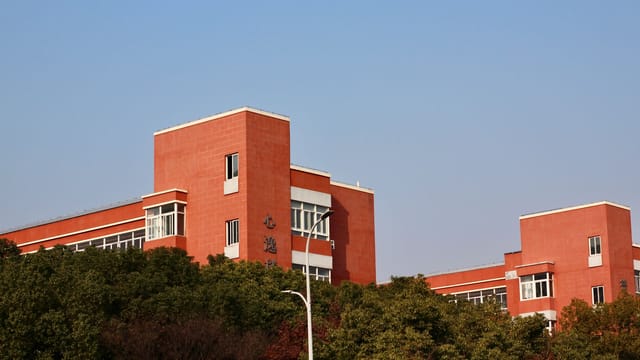 Red brick educational building surrounded by greenery under a clear blue sky.
