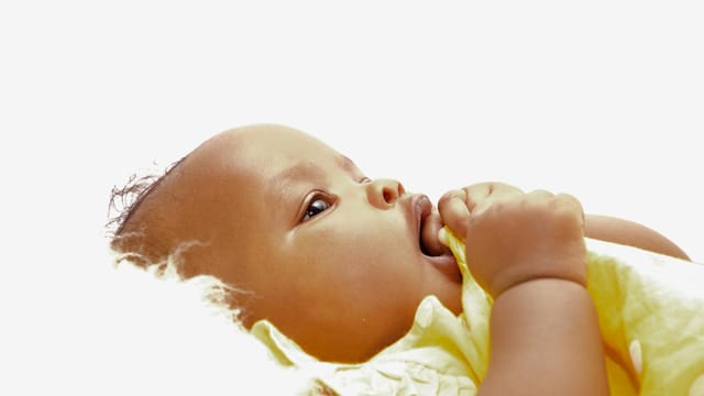 A cute baby lying down on a soft surface, holding a cloth with a serene expression.