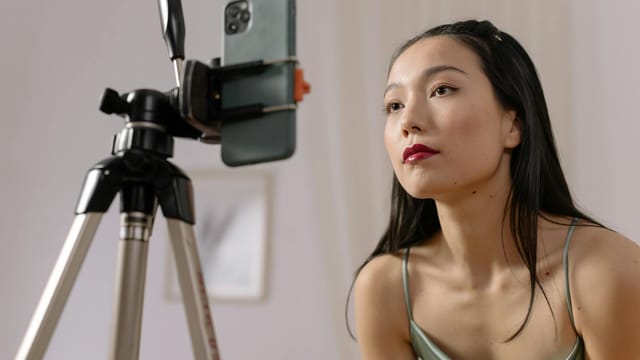 Asian woman recording a vlog indoors using a smartphone on a tripod.