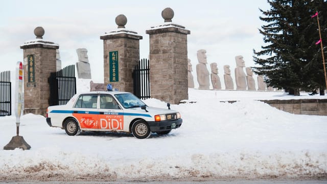 A taxi parked in snowy winter parking lot near stone statues, Japan.