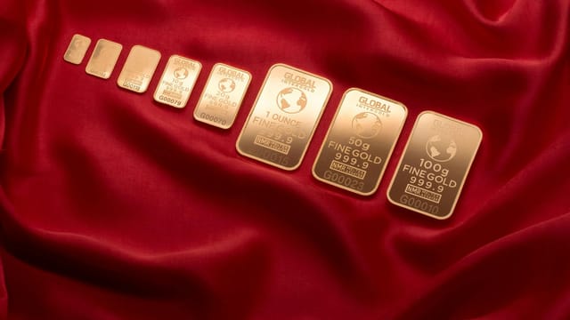 Array of fine gold bars displayed on rich red fabric, symbolizing wealth and luxury.