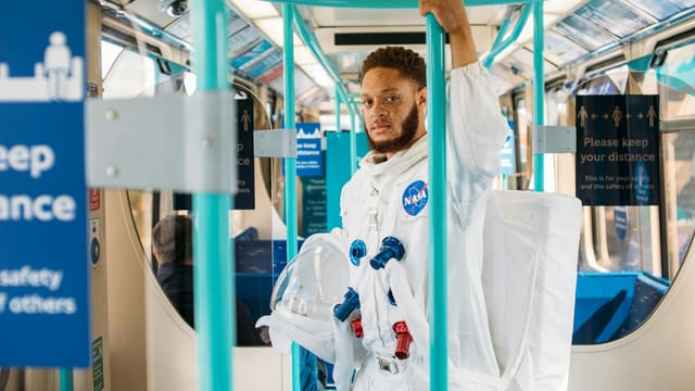 Man in astronaut suit on London subway, blending space exploration with urban life.