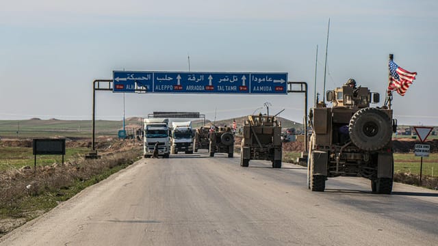 US military convoy travels on a highway in Al Hasakah, Syria, under blue skies.
