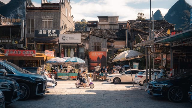 Vibrant street scene in Xingping, China featuring parked cars, motorcycles, and local shops under a sunny sky.