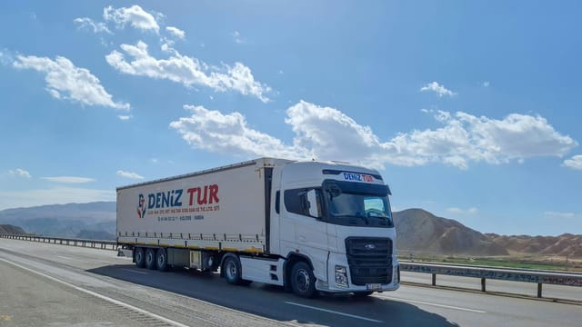 A Deniz Tur truck travels on a sunny highway in Tabriz, Iran, showcasing logistics on the road.