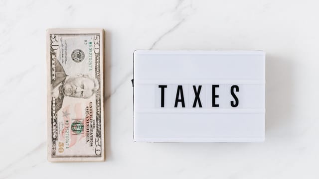 Top view composition of stack of American dollars placed on white marble surface with white retro light box with TAXES inscription