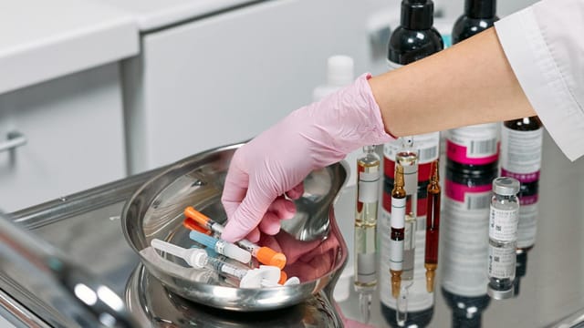 Close-up of a cosmetologist's gloved hand preparing syringes on a tray in a clinic setting.