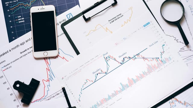Stock market analysis setup with charts, phone, magnifier, and clipboards.