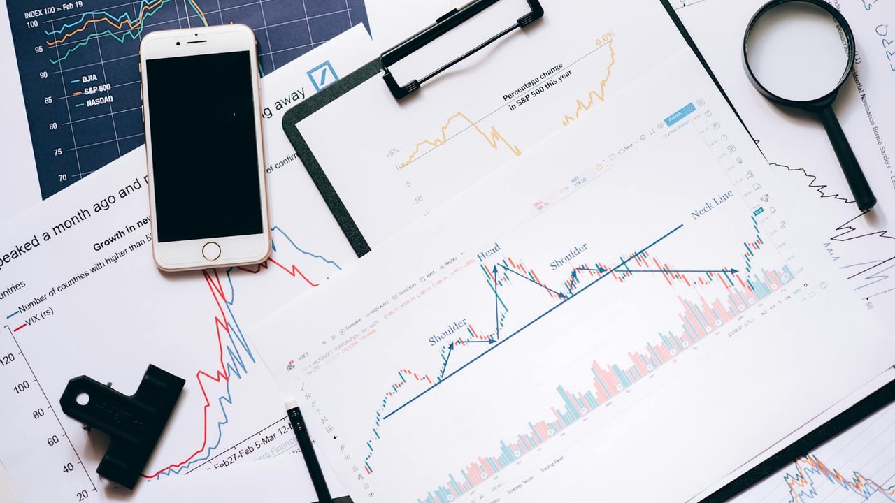 Stock market analysis setup with charts, phone, magnifier, and clipboards.